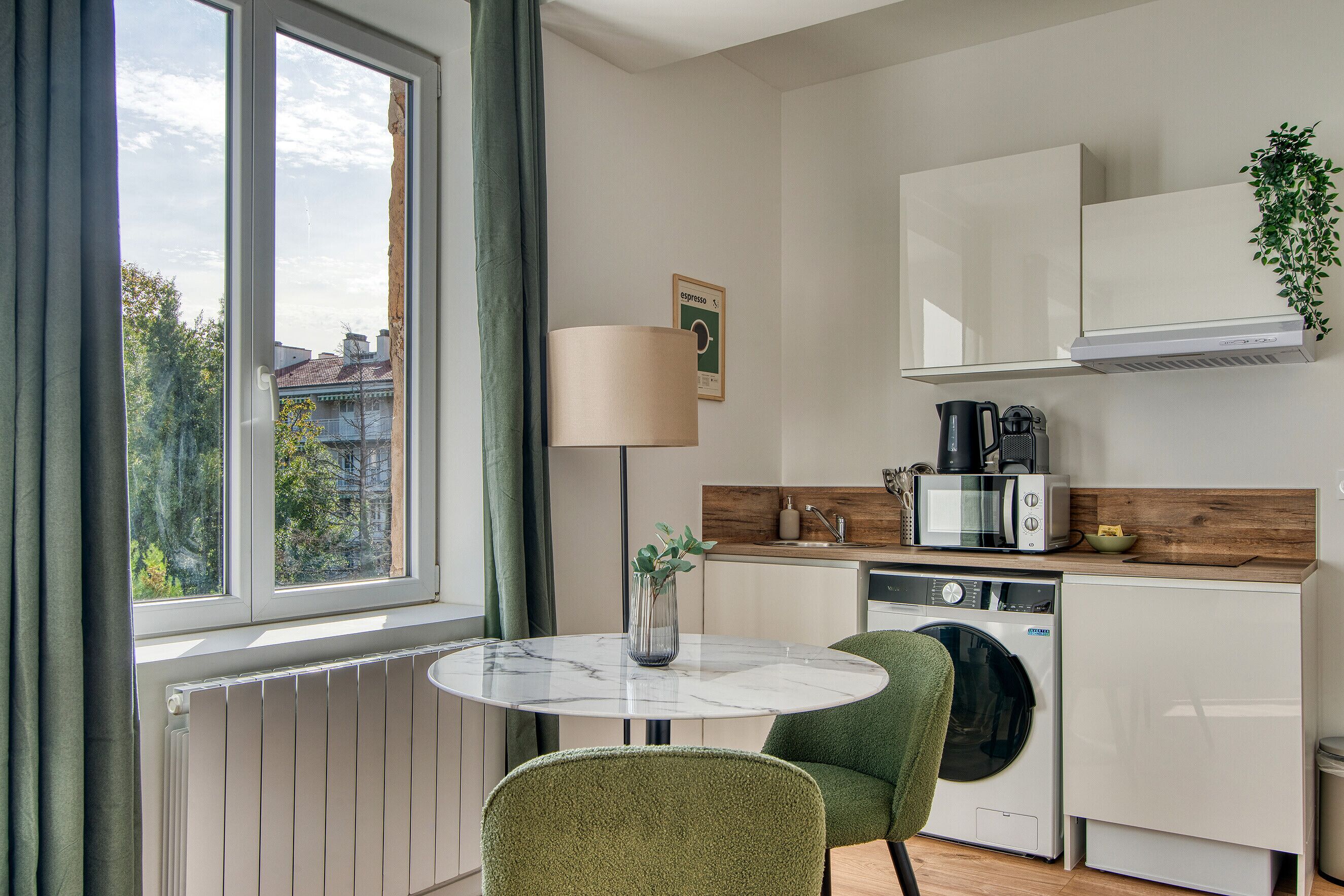 A compact kitchen with a round table, a washing machine, and a coffee maker.