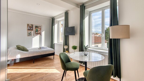 Ein modernes Zimmer mit einem Bett, einem runden Tisch und einem an der Wand befestigten Fernseher.