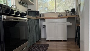 A modern kitchen with a stainless steel stove, microwave, and coffee maker on the counter. There are white cabinets and a window with blinds.
