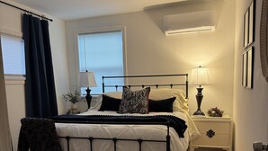A bedroom with a bed, bedside tables, a lamp, a window with blinds, and a door.