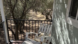 A wooden deck with two white chairs and a bench, surrounded by trees.