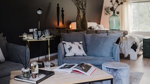 Een woonkamer met een grijze bank, een salontafel met een boek en een kaars, en een bijzettafeltje met decoratieve objecten.