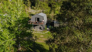 Een modern huis met twee verdiepingen, een terras en een overdekte buitenruimte, omgeven door weelderige begroeiing.