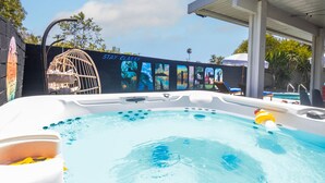 Un jacuzzi con un mural de fondo, una zona techada con sillones de descanso y una piscina.
