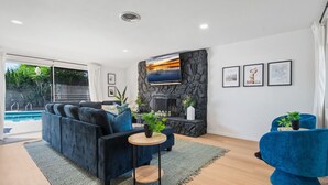Una sala moderna con chimenea de piedra, un televisor grande y vista a una piscina.