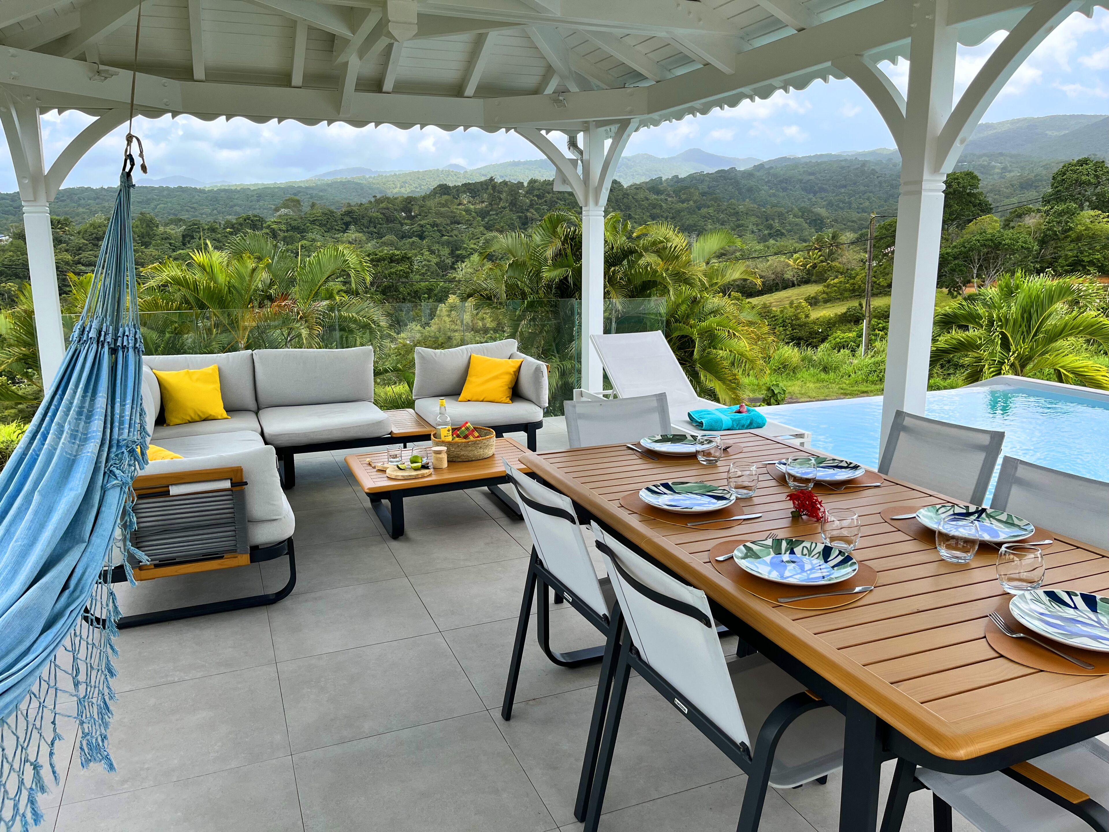 A covered outdoor seating area with a pool, a hammock, and a table set for dining.