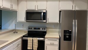 A modern kitchen with white cabinets, a stainless steel refrigerator, a microwave, and an oven.