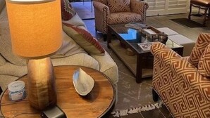 A living room with a sofa, patterned armchairs, a coffee table, a lamp, and a view of a tree through a glass door.
