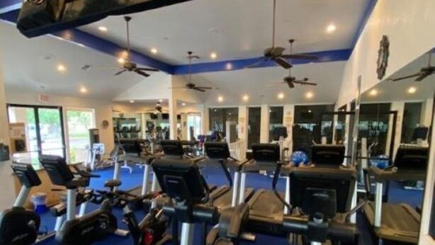 A gym with various cardio machines, mirrors, and ceiling fans.