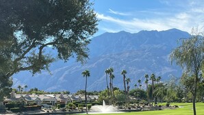 A well-maintained golf course with a fountain, palm trees, and a mountain backdrop.