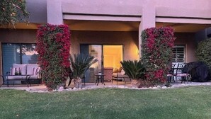A building with a patio area featuring outdoor furniture, a covered barbecue, and lush greenery.