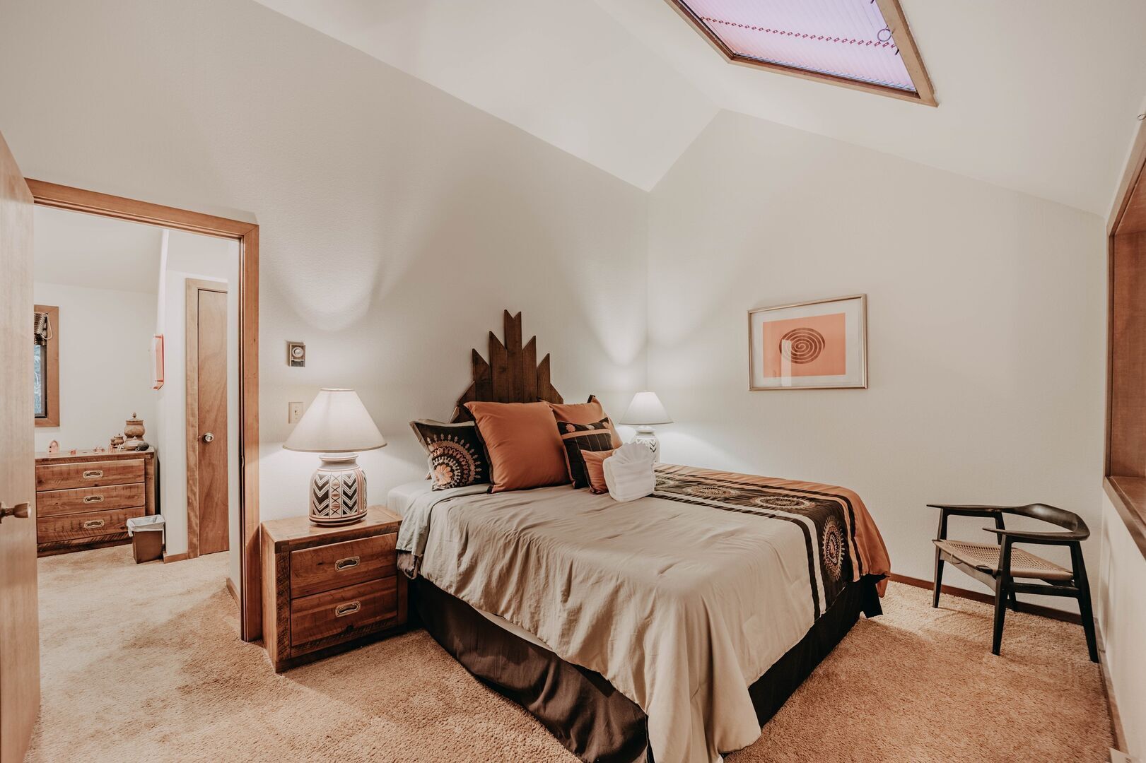 A bedroom with a bed, nightstands, a dresser, a chair, and a skylight.