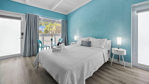 A modern bedroom with a large bed, a bedside table with a lamp, and a view of the outdoors through a sliding door. - Chic Hotel in Vibrant Miami with Free Pool, WiFi, Coffee and Bagels - BOOK NOW! (Miami)
