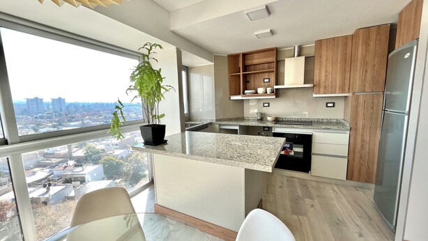 Una cucina moderna con vista sulla città, armadietti in legno, un frigorifero in acciaio inossidabile e una pianta in vaso.