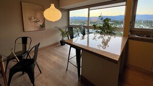 Una cucina moderna con una grande isola, un'area pranzo con sedie, una lampada a sospensione e vista sulla città attraverso ampie finestre.