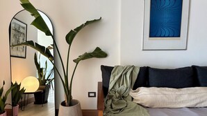 Un soggiorno moderno con un grande specchio, una pianta in vaso, un quadro astratto incorniciato e un letto rifatto con cura.
