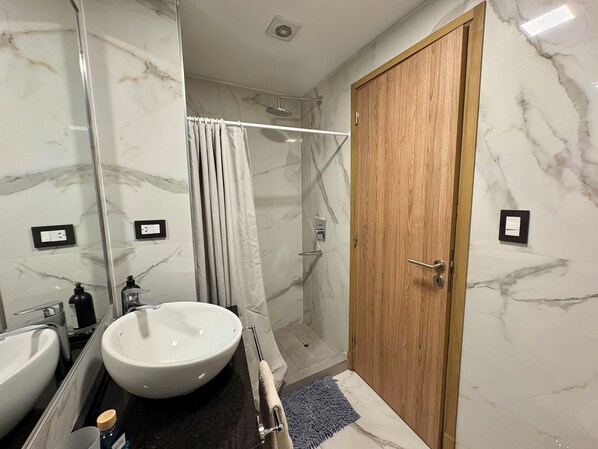 Une salle de bain avec un mur en marbre, une porte en bois, un lavabo blanc, une douche et un porte-serviettes.