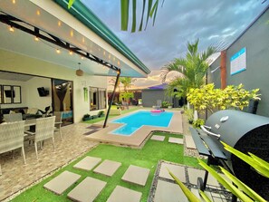 Ein Garten mit Schwimmbad, Gartenmöbeln und Grill.