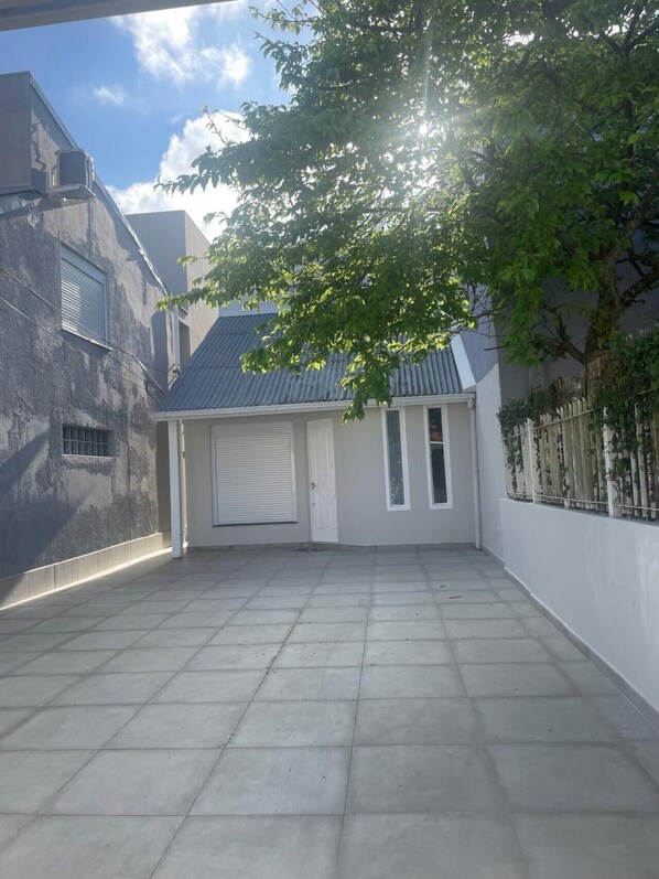 A courtyard with a tiled floor, a garage door, and a tree providing shade. - Casa ao Lado da Praia de Canasvieiras (Florianópolis)