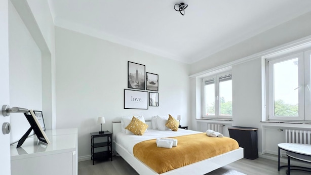 Een moderne hotelkamer met een groot bed, een wit vloerkleed en ingelijste foto’s aan de muur.