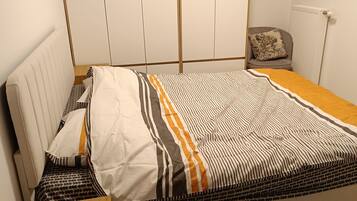 Ein Schlafzimmer mit einem Bett, einem Holznachttisch, einem Stuhl, einem gemusterten Teppich und einer Heizung.