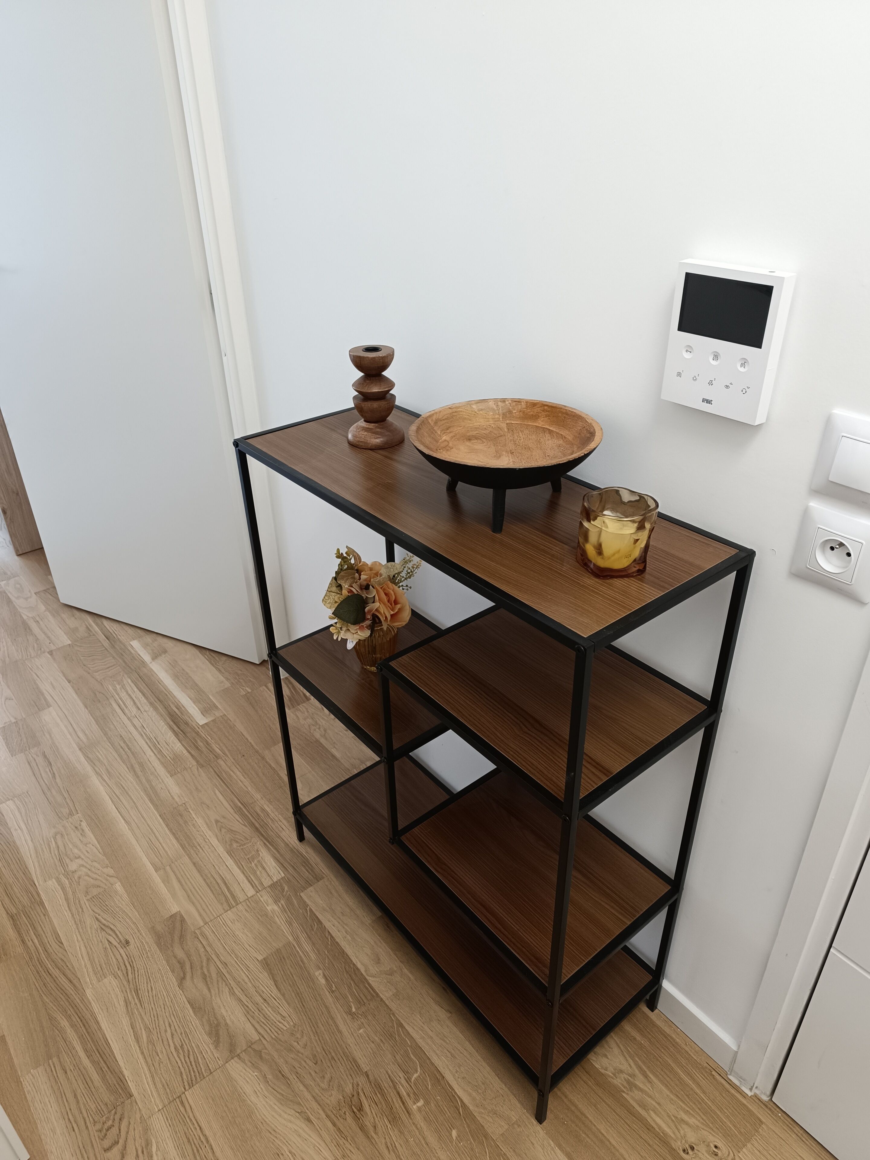 Een houten console tafel met een rond blad en één plank, een kleine vaas met gedroogde bloemen, en een glas water.
