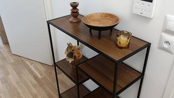 Een houten console tafel met een rond blad en één plank, een kleine vaas met gedroogde bloemen, en een glas water.