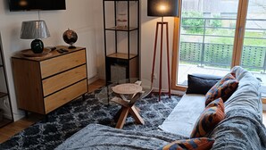 Moderni makuuhuone, jossa on suuri sänky, puinen lipasto, lasipöytä ja seinälle asennettu televisio.