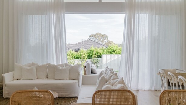 Una habitación con sofá blanco, sillas de mimbre y cortinas translúcidas.
