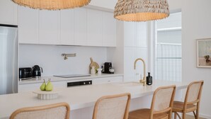 Una cocina moderna con armarios blancos, una isla central con sillas, una cafetera y una lámpara colgante.