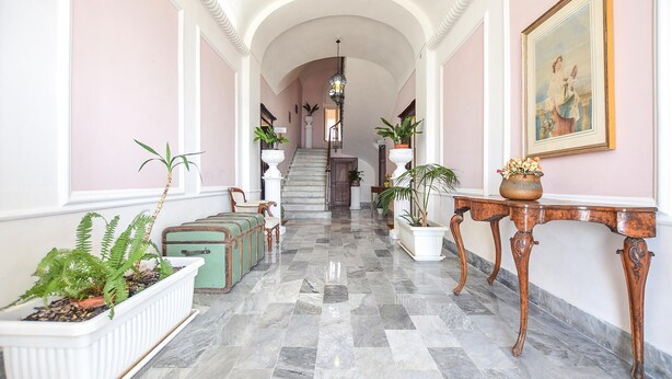 A hallway with a marble floor, a staircase, potted plants, vintage suitcases, and a painting on the wall. - Amazing apartment in Santa Maria di Castell (Santa Maria di Castell)