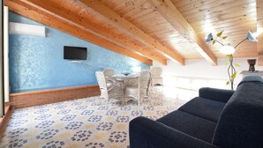 A room with a wooden ceiling, a blue wall, a TV mounted on the wall, a dining table with chairs, and a sofa. - Amazing apartment in Santa Maria di Castell (Santa Maria di Castell)
