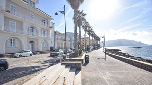 A coastal promenade with buildings, palm trees, and a stone wall. - Amazing apartment in Santa Maria di Castell (Santa Maria di Castell)