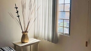 Une pièce avec une fenêtre, un vase rempli de branches et un coussin à rayures.