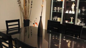 Un coin repas avec une table à plateau en verre, des chaises noires et un vase contenant des plantes séchées.