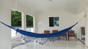 Quarto com rede, cadeiras de madeira, janela e porta que dá para o exterior.