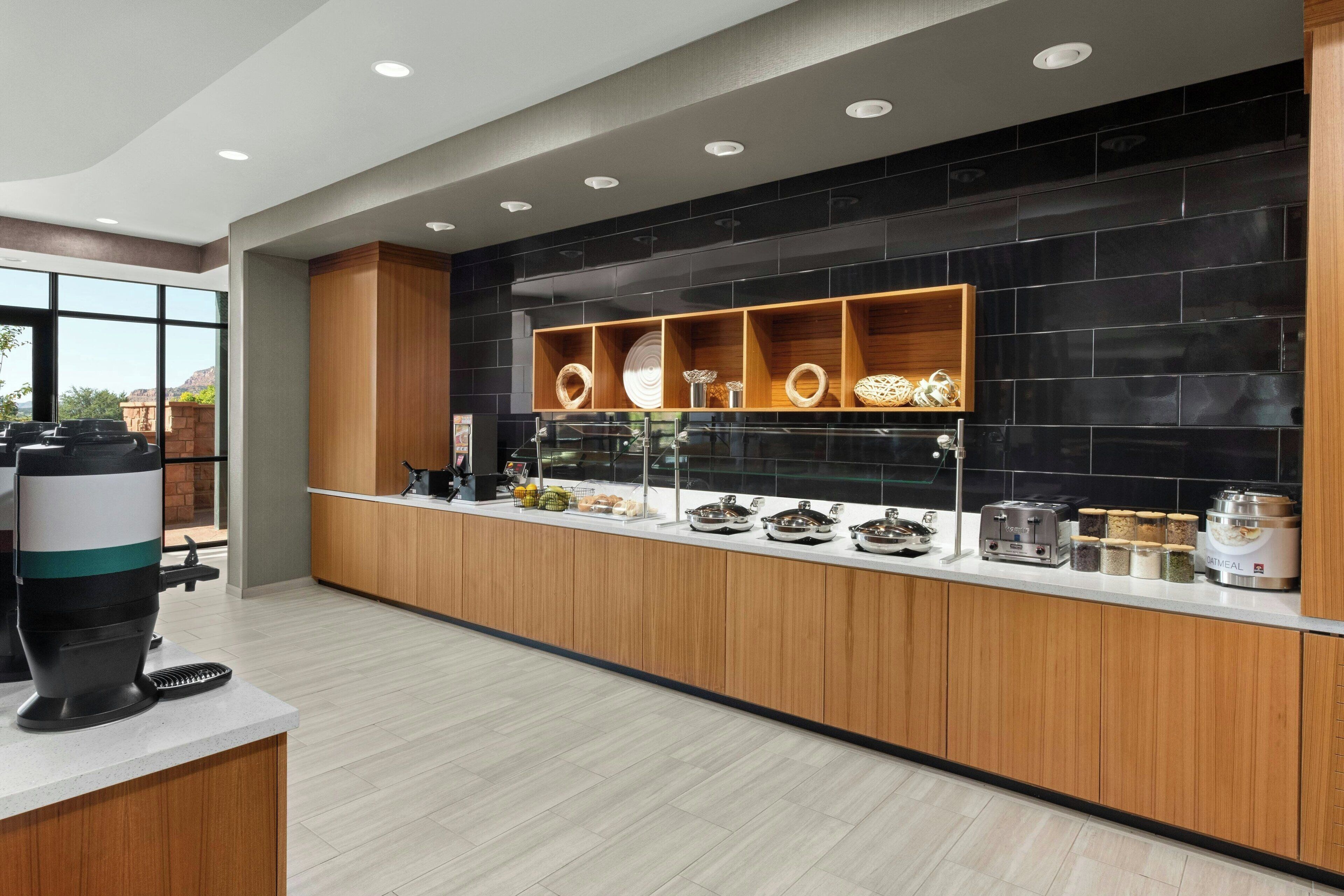 Une cuisine moderne avec un mur recouvert de carreaux noirs, des meubles en bois et un buffet où sont disposés divers aliments et appareils de cuisine.
