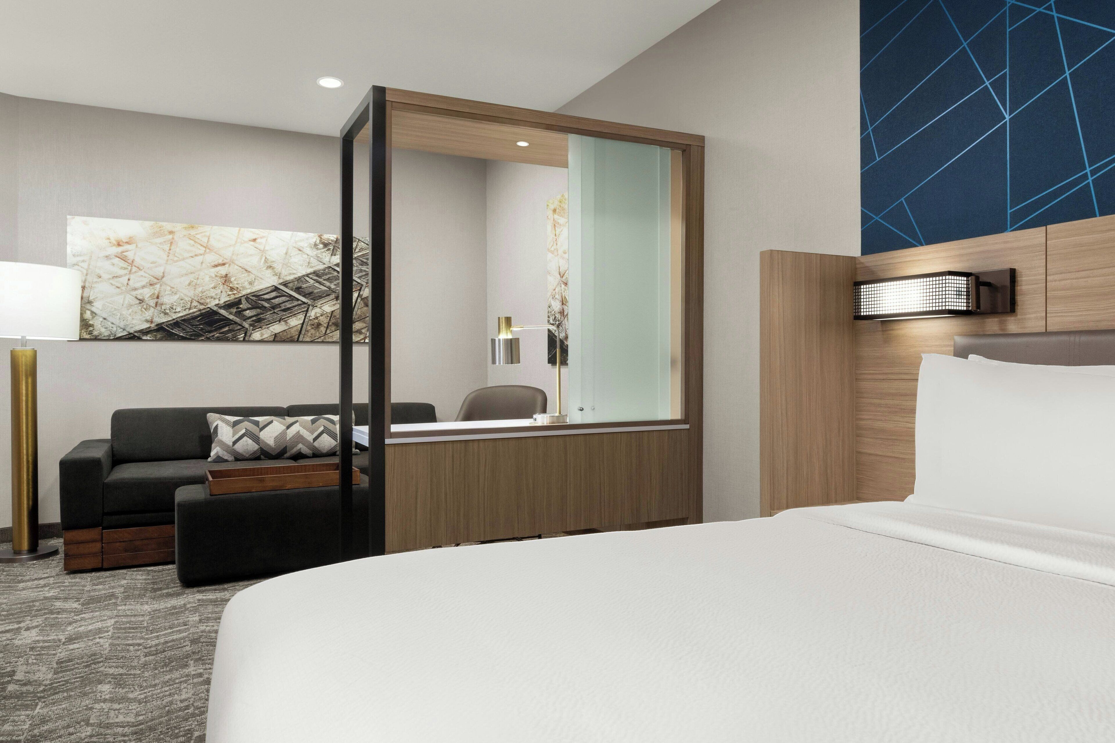 Una habitación de hotel moderna con una cama grande, un sofá, un escritorio y un espejo amplio.