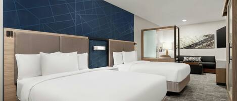 A hotel room with two beds, a large mirror, a sofa, and a wall with a geometric pattern.