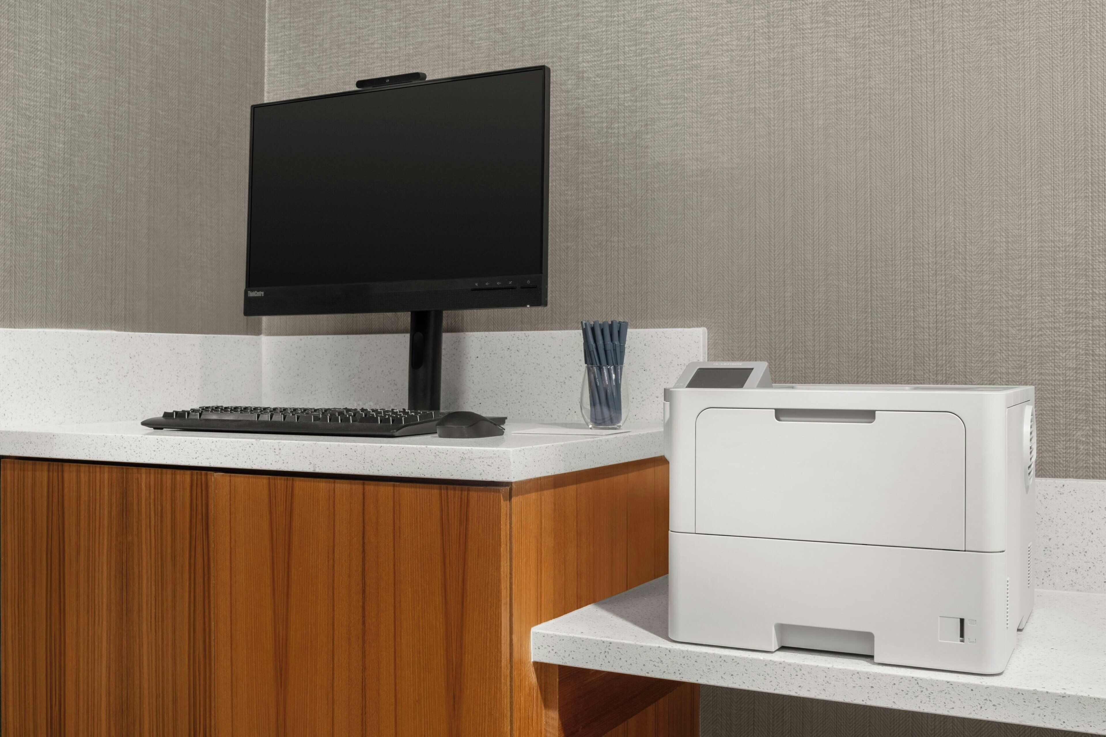 A modern office setup with a flat-screen monitor, keyboard, and a white printer on a speckled countertop.