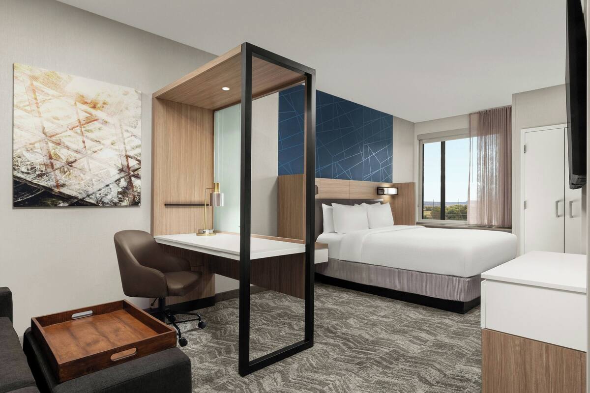 Ein Hotelzimmer mit Bett, Schreibtisch, Stuhl und einem großen Spiegel.