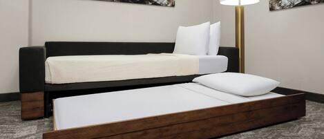 Un lit avec un cadre en bois, un matelas blanc et un oreiller blanc. Une lampe de sol à abat-jour blanc se trouve à côté du lit.