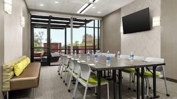 A conference room with a long table, chairs, a bench, and a TV on the wall.