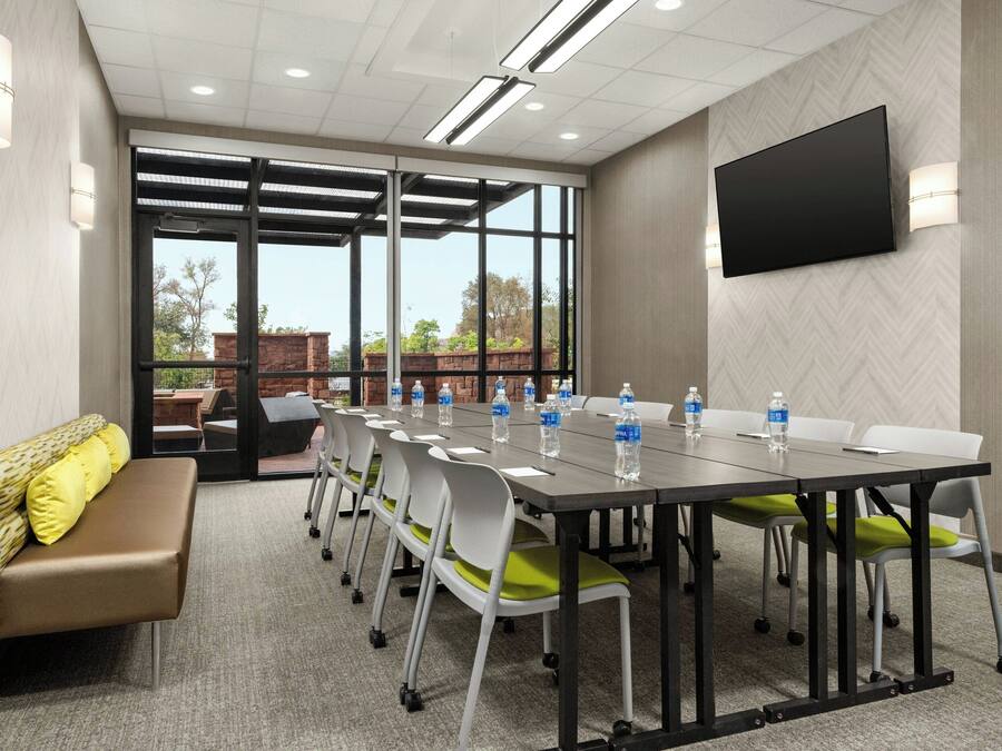 A conference room with a long table, chairs, a bench, and a TV on the wall.