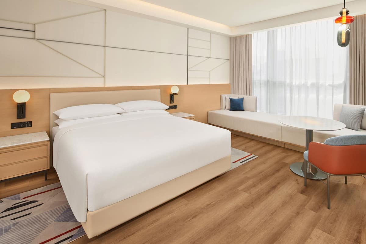 A modern hotel room with a large bed, a sofa, a small table, and a chair.