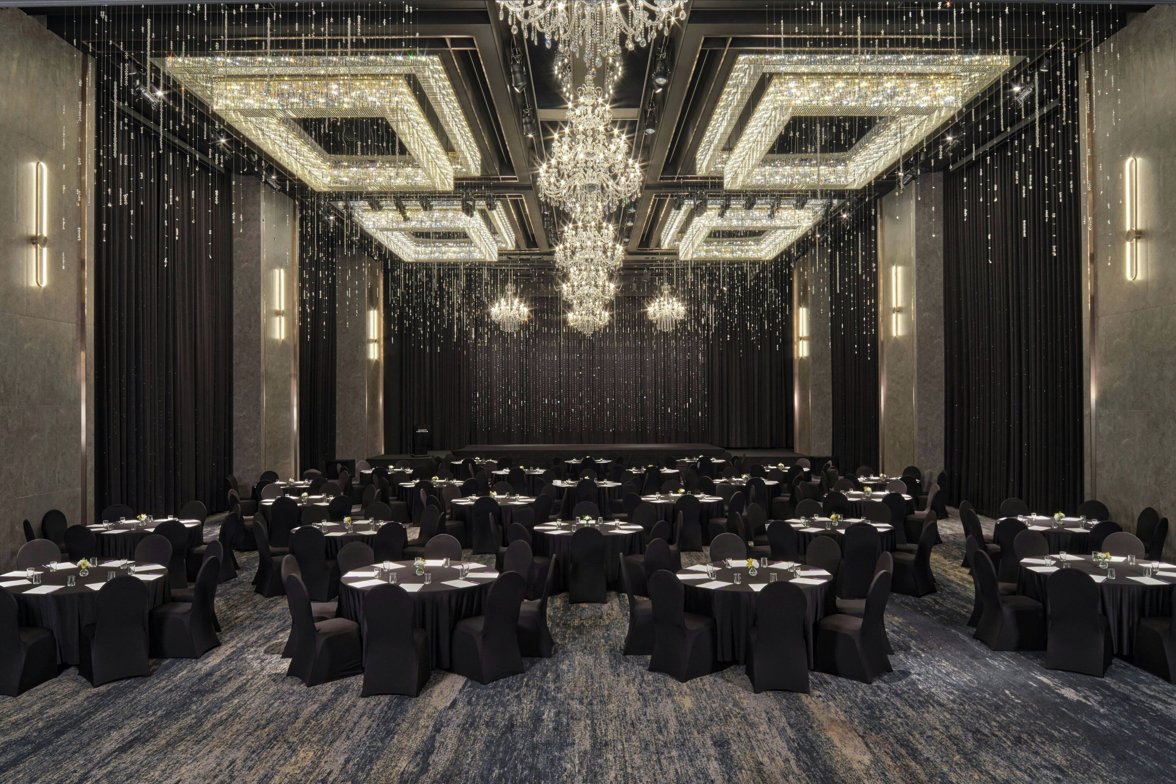 A large conference room with rows of tables and chairs, a central chandelier, and a patterned carpet.