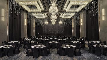 A large conference room with rows of tables and chairs, a central chandelier, and a patterned carpet.