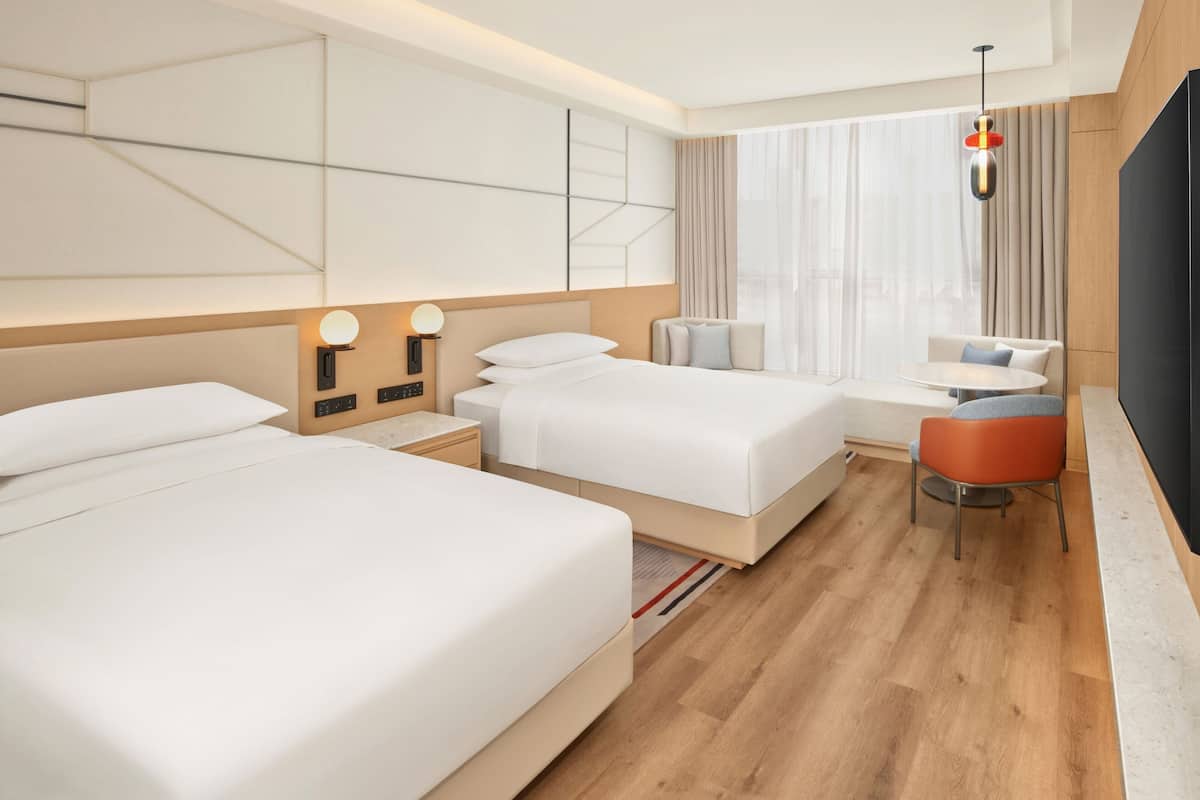 A hotel room with two beds, a desk, a chair, a TV, and a large window with curtains.