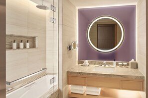 Ein modernes Badezimmer mit Duschkabine aus Glas, einem Waschtisch mit Marmorplatte und einem großen Spiegel mit runder Beleuchtung.