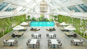A spacious indoor pool area with multiple seating options, including lounge chairs and tables, surrounded by greenery and a clear view of the sky through a glass ceiling. - The Link Seoul, A Tribute Portfolio Hotel (Seoul)